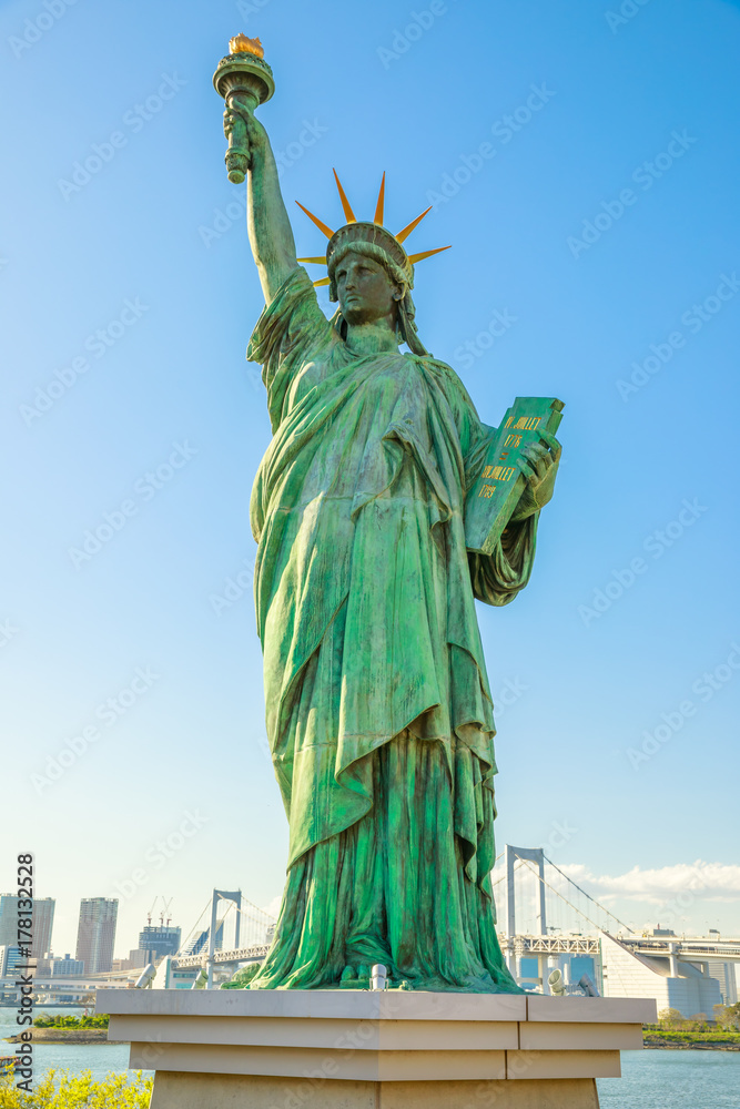 Obraz premium Statua Wolności, ikony wyspy Odaiba w Tokio, Japonia. Replika słynnej Statuy Wolności Nowego Jorku. Tokio pejzaż i tęczowy most na tle. Pionowe ujęcie w błękitne niebo.
