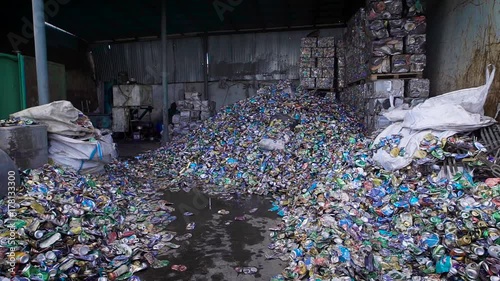 many of old used aluminum cans are lying on a floor of huge shed and pressed briquettes of metal scrap are standing photo