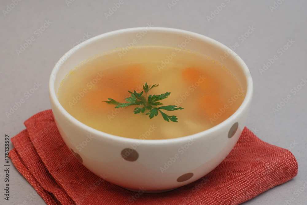 Spicy homemade soup served in pottery bowl with orange napkin on gray background Spicy homemade soup served in pottery bowl with orange napkin on gray background