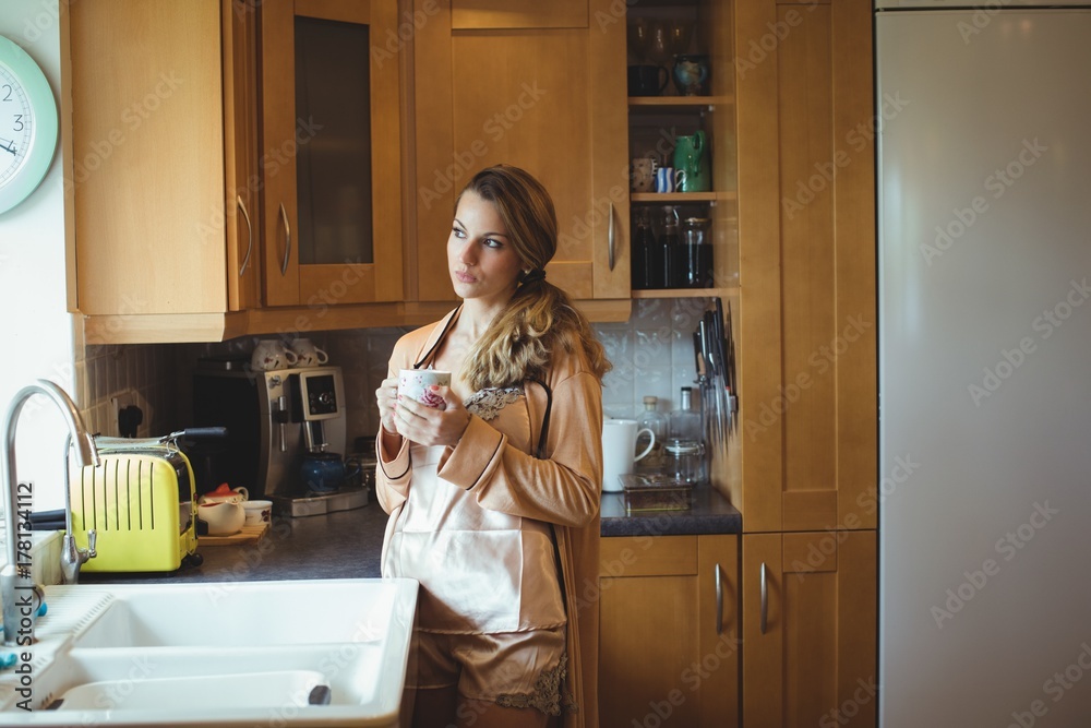 Thoughtful woman holding coffee cup in kitchen Thoughtful woman holding coffee cup in kitchen