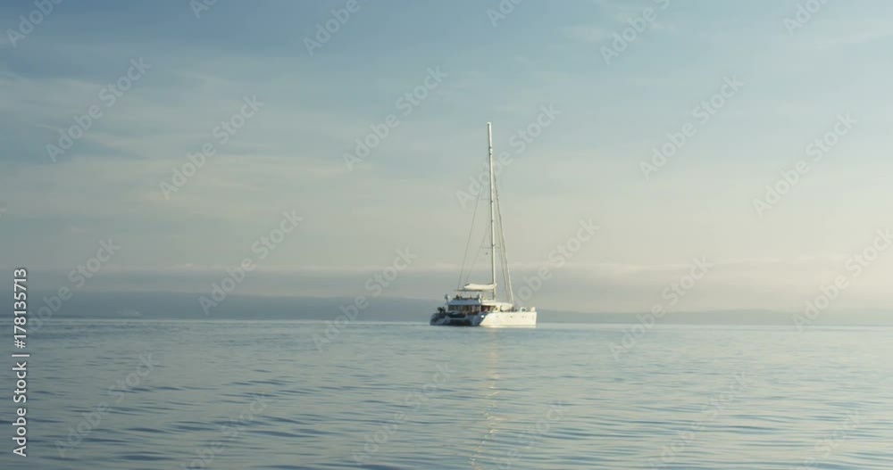 White Catamaran Yacht Sailing on a Beautiful Azure Sea with Land in the Background. Shot on RED Epic 4K UHD Camera. White Catamaran Yacht Sailing on a Beautiful Azure Sea with Land in the Background. Shot on RED Epic 4K UHD Camera.