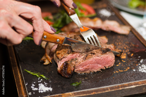 Woman hand holding knife and fork cutting grilled beef steak