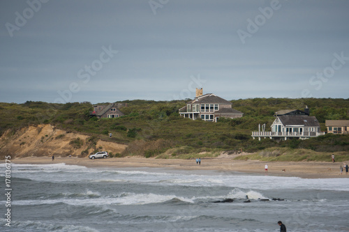 Obraz na płótnie Wide exterior view of beachfront luxury vacation homes along the ocean coastline on a summer day. Rough surf waves splash along the sand w salonie