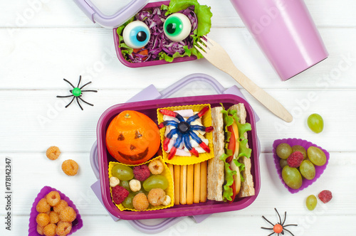 Open Halloween lunch box with school lunch on white wooden background