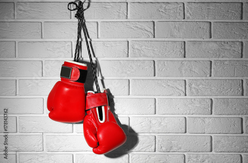 Pair of red boxing gloves hanging on brick wall © Africa Studio