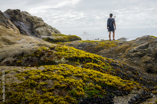 A hiker is standing and looking out to sea stack.