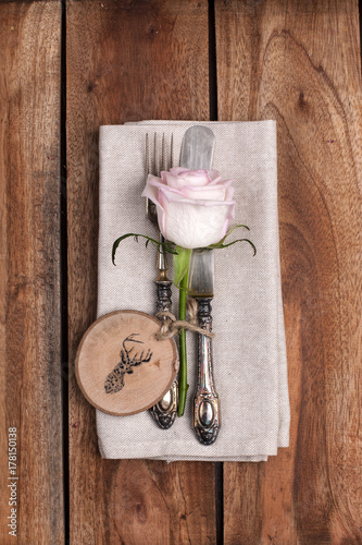 a wooden table is served with cutlery and a white rose