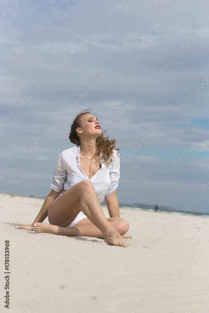 Young cute woman sitting on sand wear bottom white bikini and tied shirt Young cute woman sitting on sand wear bottom white bikini and tied shirt