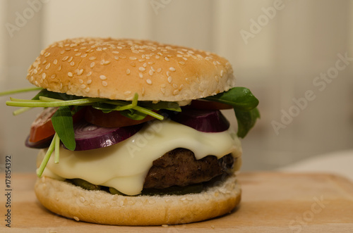 Delicious homemade hamburger served with French fries on wooden background. Delicious burger with onion, tomato, cheese and lettuce. Fast food meal. Rustic style.