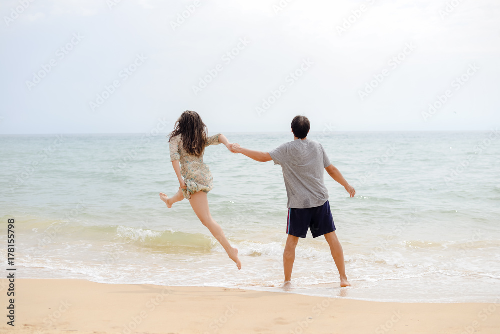 Adult young happy jumping couple on seashore outdoors nature sand background. Back view of pretty romantic lovers having fun holding hands in tenderness bliss moment. destination trip