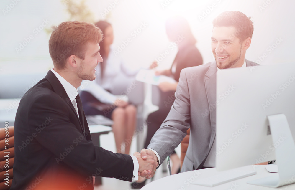 Fototapeta premium Two happy young men shaking hands while sitting at the office