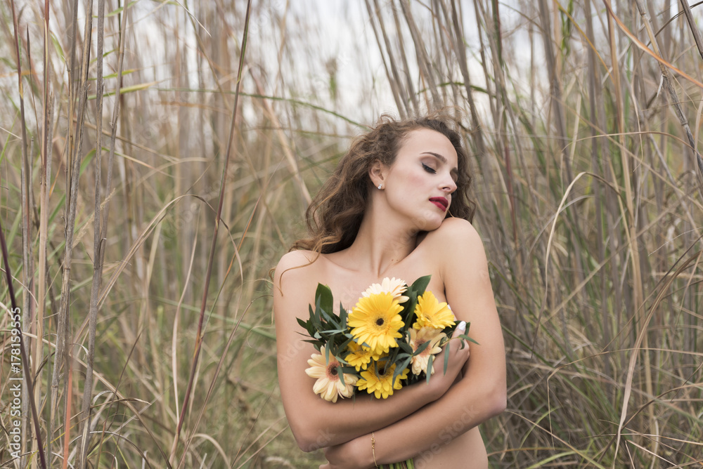 Young pretty woman with curly long hair hugging a bouquet of flowers, outdoor shot in dry long grass Young pretty woman with curly long hair hugging a bouquet of flowers, outdoor shot in dry long grass