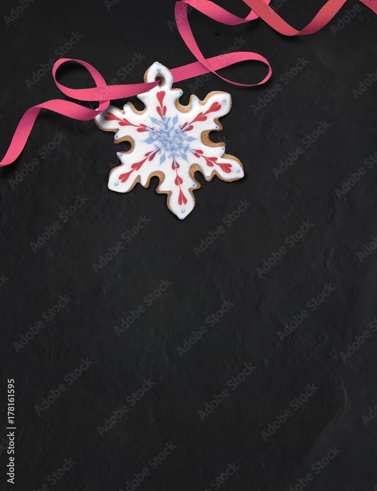 Snowflake-shaped gingerbread cookie on black slate background. Decorated with royal icing in white, red and blue. Top down view. Snowflake-shaped gingerbread cookie on black slate background. Decorated with royal icing in white, red and blue. Top down view.