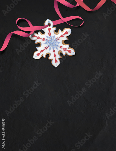 Snowflake-shaped gingerbread cookie on black slate background. Decorated with royal icing in white, red and blue. Top down view.