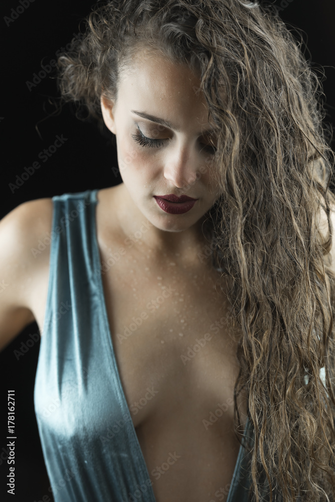 Fototapeta premium Wet look from a cute woman, studio in black background, wet skin and hair, wear blue shine one piece swimsuit