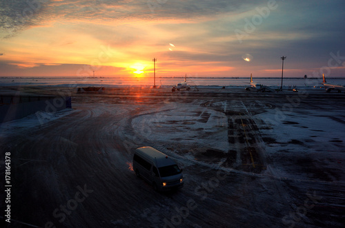 at the airport: snow-covered asphalt runway and on it there is an airplane on the foyer of sunset or dawn and bright sky and car driving © sibiranna