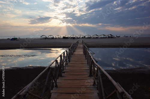 the girl goes off into the distance to the sunset ocean and the beach along a long wooden bridge © sibiranna