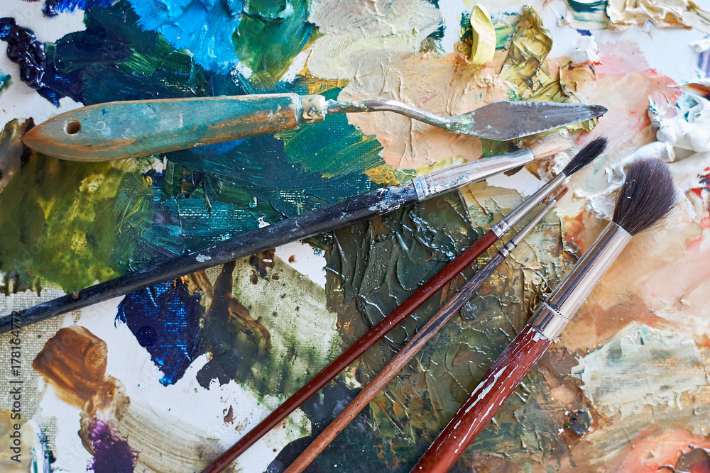 Artistic brushes and stacks lie on a palette with paints