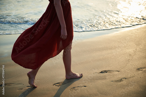 barefoot girl in red dress walking along the beach