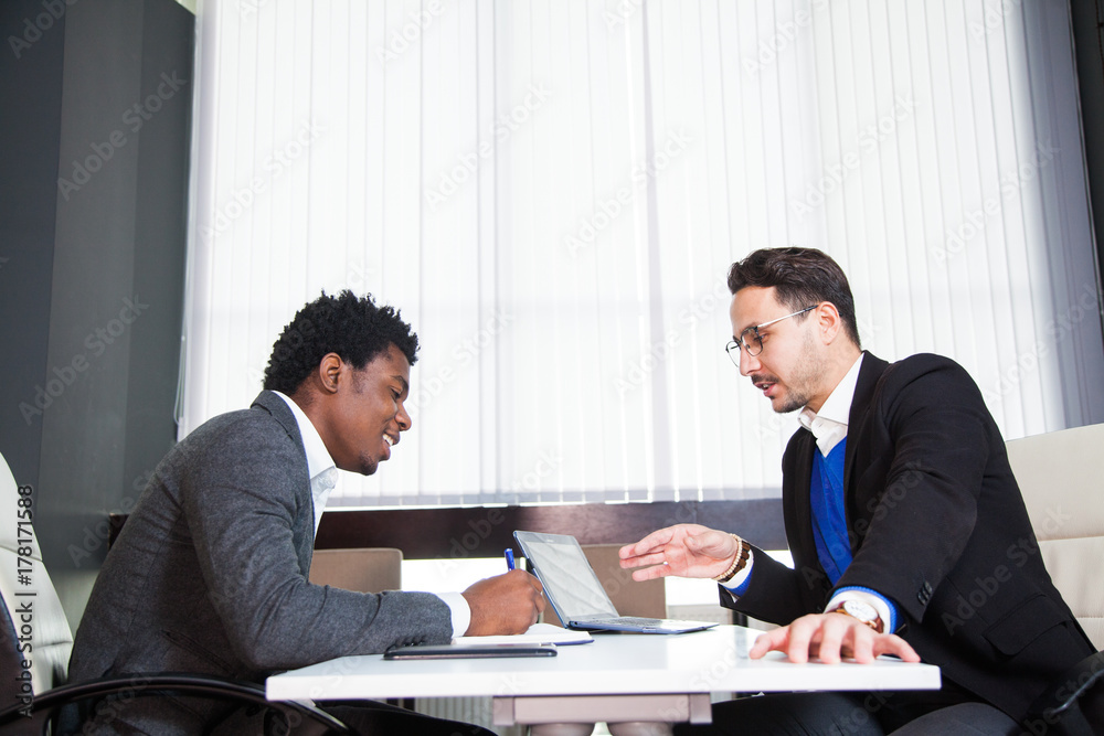 Two young businessmen, white desk, job interview, teamwork. Two successful male entrepreneurs at office work together Two young businessmen, white desk, job interview, teamwork. Two successful male entrepreneurs at office work together