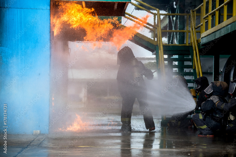 Fototapeta premium Firemen using water from hose for fire fighting at firefight training of insurance group. Firefighter wearing a fire suit for safety under the danger case.