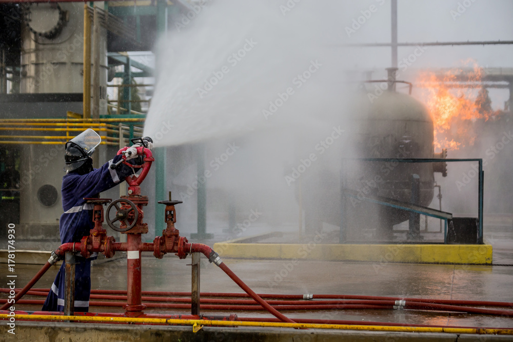 Fototapeta premium Firemen using water from hose for fire fighting at firefight training of insurance group. Firefighter wearing a fire suit for safety under the danger case.