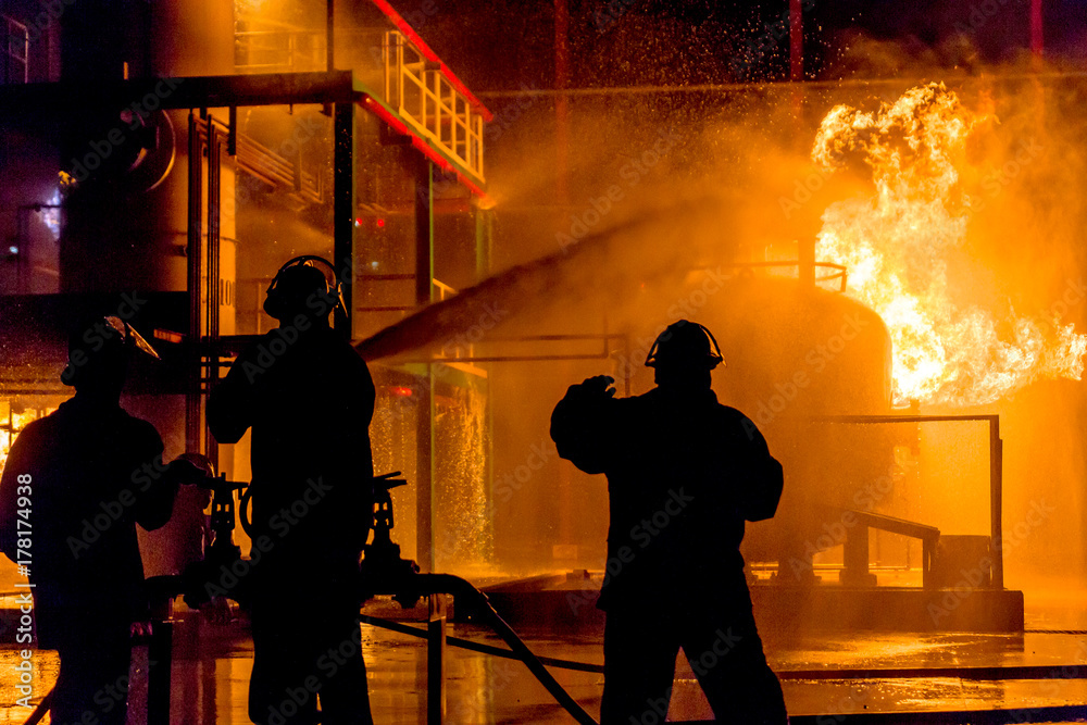 Fototapeta premium Firemen using water from hose for fire fighting at firefight training of insurance group. Firefighter wearing a fire suit for safety under the danger case.