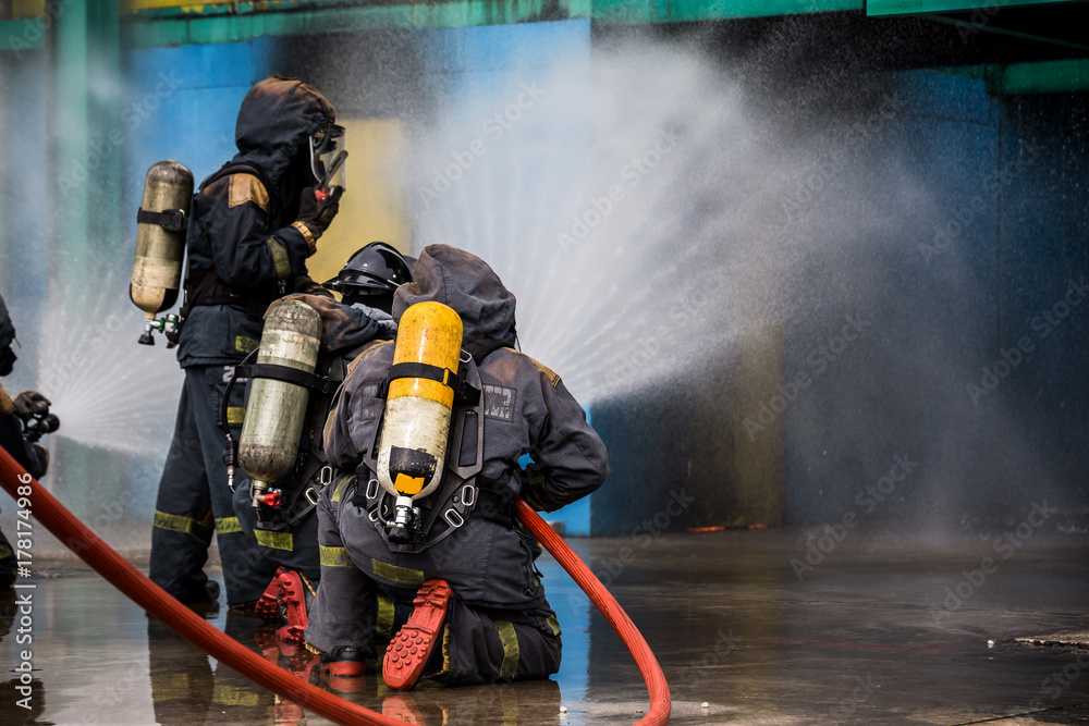 Fototapeta premium Firemen using water from hose for fire fighting at firefight training of insurance group. Firefighter wearing a fire suit for safety under the danger case.