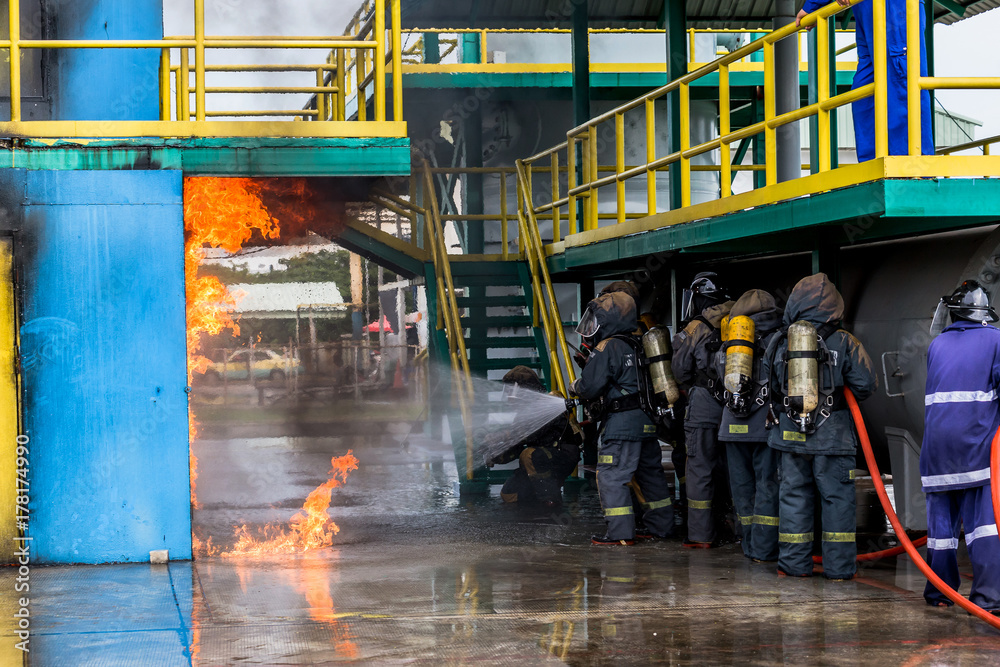 Fototapeta premium Firemen using water from hose for fire fighting at firefight training of insurance group. Firefighter wearing a fire suit for safety under the danger case.