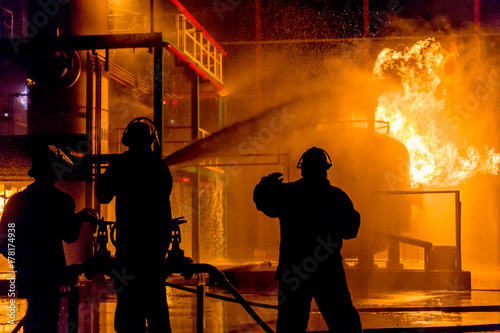 Firemen using water from hose for fire fighting at firefight training of insurance group. Firefighter wearing a fire suit for safety under the danger case.