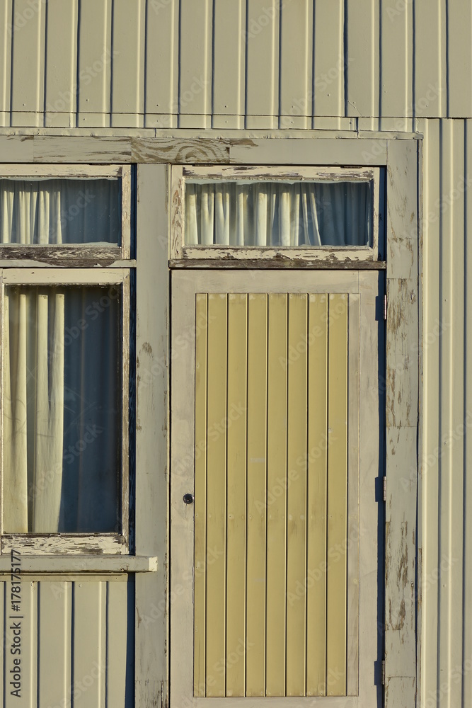 Door and window detail of weathered house with wooden cladding on outer walls.