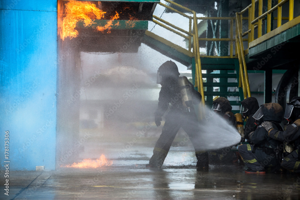 Fototapeta premium Firemen using water from hose for fire fighting at firefight training of insurance group. Firefighter wearing a fire suit for safety under the danger case.