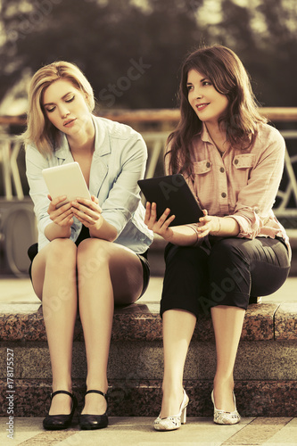 Two young fashion women using tablet computers outdoor