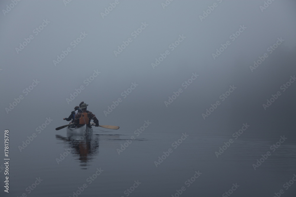 Fototapeta premium People canoeing on a misty day through dense fog