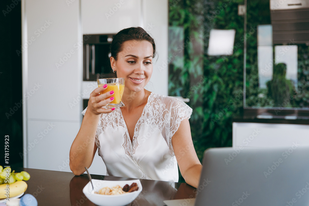 Portrait of beautiful young woman working with laptop while breakfast with cereals and milk and drinking orange juice. Eating at home. Portrait of beautiful young woman working with laptop while breakfast with cereals and milk and drinking orange juice. Eating at home.
