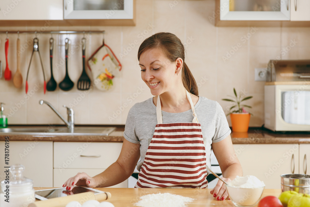 A young beautiful happy woman looking for a recipe for Christmas cakes in tablet in the kitchen. Cooking home. Prepare food. A young beautiful happy woman looking for a recipe for Christmas cakes in tablet in the kitchen. Cooking home. Prepare food.