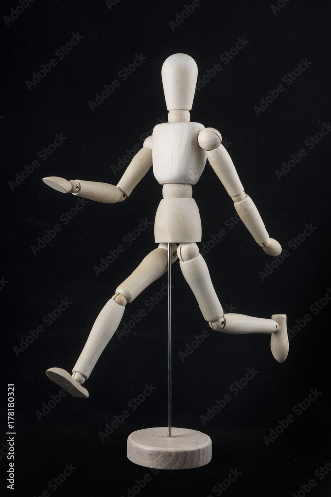 a wooden dummy posing while running with a black background a wooden dummy posing while running with a black background