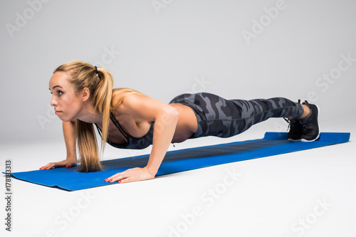 Young attractive woman practicing yoga, doing Push ups or press ups exercise, Plank pose, working out, wearing sportswear, red tank top, pants, indoor full length, isolated, grey studio background photo