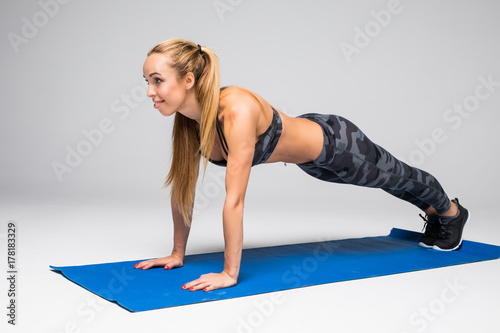 Young attractive woman practicing yoga, standing in Push ups or press ups exercise, Plank pose, working out, wearing sportswear bra and pants, full length, gray studio background photo