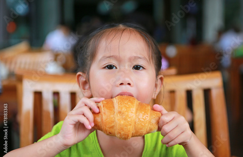 Cute little girl eating croissant at restaurant on the morning.