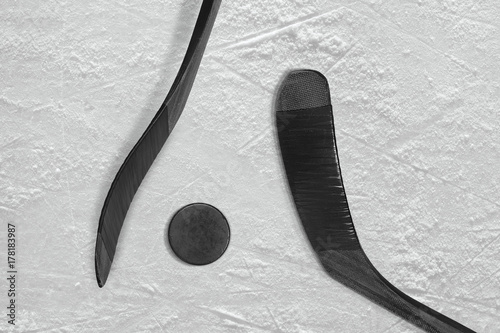 Two black sticks and ice hockey puck