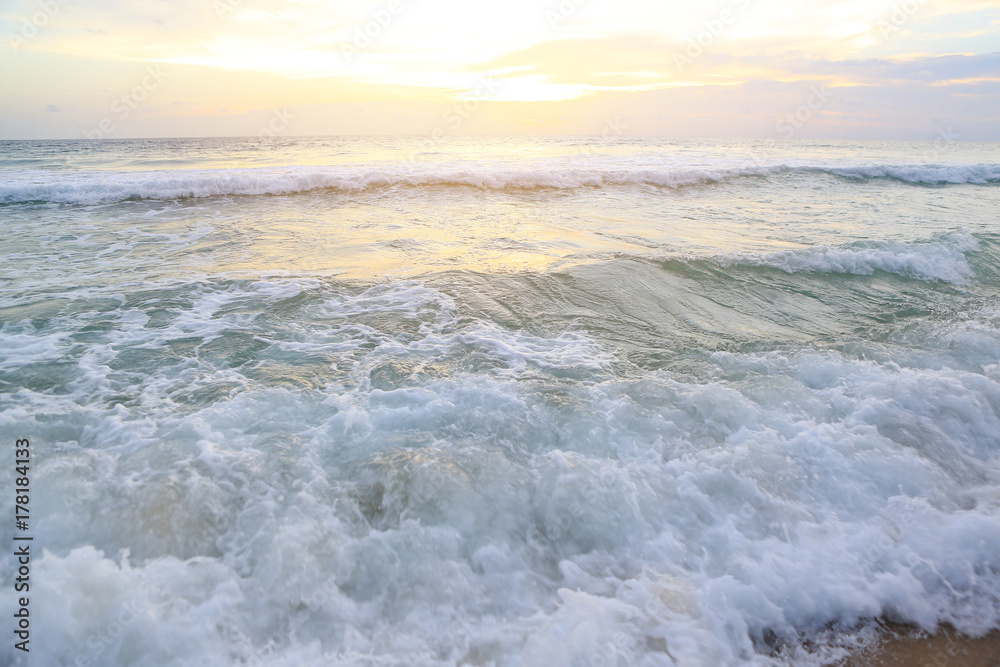 Shiny tropic sea wave on golden beach sand in sunset light.