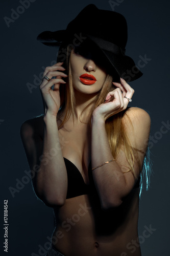 vertical portrait of slim young girl in black bra with red lips wearing a hat with wide brim in studio © ponomarencko