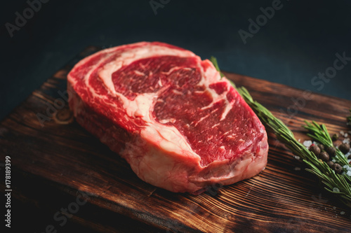 raw rib eye steak on a wooden Board on black background - rustic stule