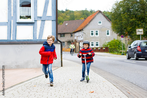Two little schoolkids boys running and driving on scooter on autumn day © Irina Schmidt