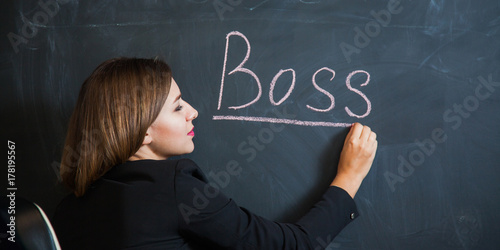 Business woman writing the word boss on desk. Female office worker put down text on black board. Banner