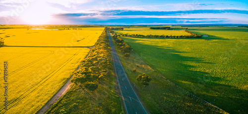 Aerial panorama of rural road passing through agricultural land in Australian countryside at sunset