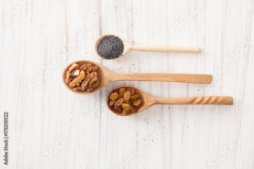 Raisins, nuts and poppy seeds in wooden spoons on white