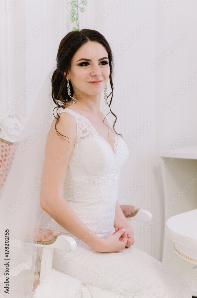 Beautiful bride perfect style. Wedding hairstyle make-up dress and bride's bouquet. Young attractive bride on chair in white room at studio Beautiful bride perfect style. Wedding hairstyle make-up dress and bride's bouquet. Young attractive bride on chair in white room at studio