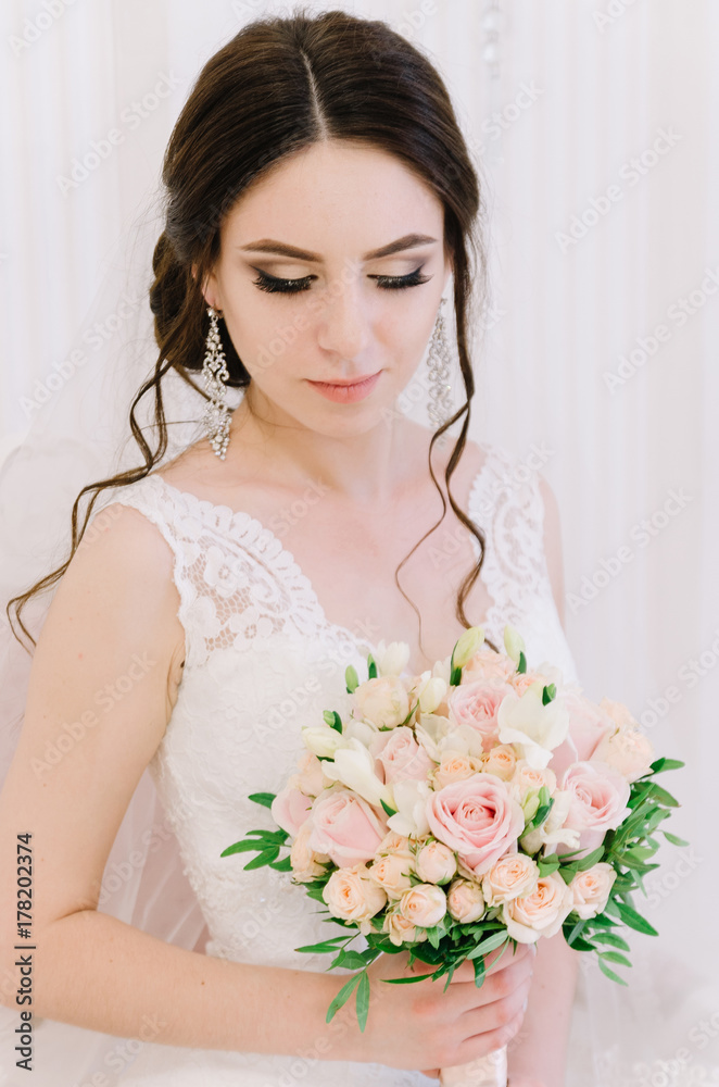 Beautiful bride perfect style. Wedding hairstyle make-up dress and bride's bouquet. Young attractive bride on chair in white room at studio Beautiful bride perfect style. Wedding hairstyle make-up dress and bride's bouquet. Young attractive bride on chair in white room at studio